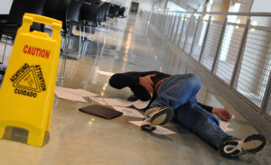 A man who slipped on a wet floor beside a bright yellow caution sign holds his back in pain ** Note: Shallow depth of field