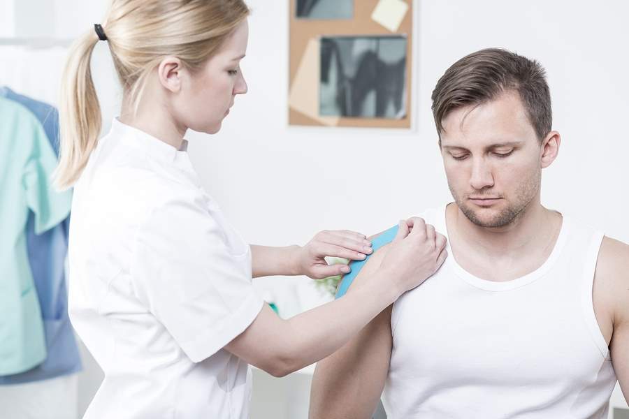 Physiotherapist applying kinesiology tape for painful shoulder