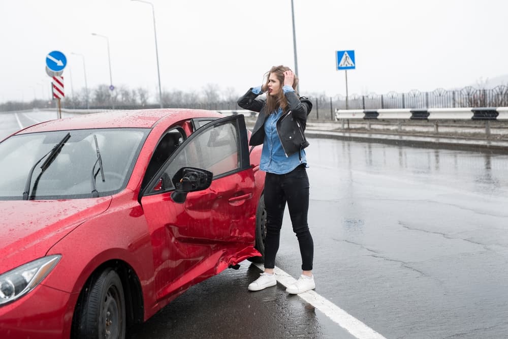 Female driver near damaged car in Columbus, Ohio, seeking assistance after an accident.
