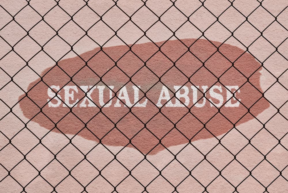 Text Sexual Abuse written under a wire fence