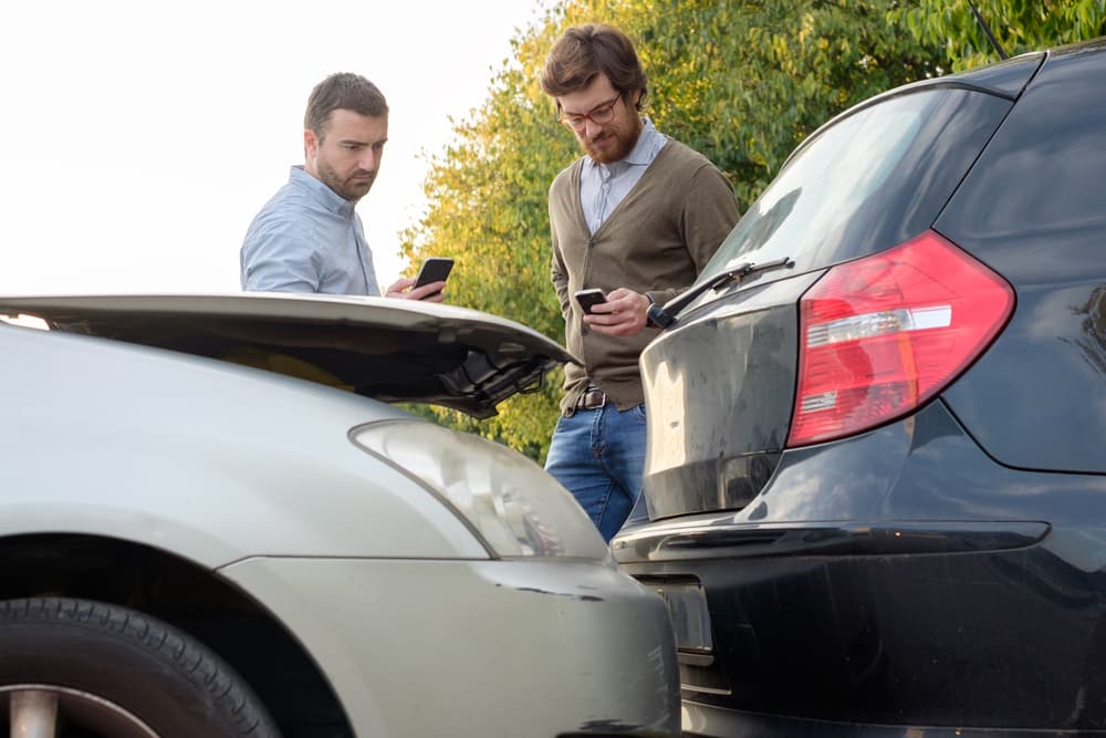 Hombres llamando a asistencia de seguro mecánico de automóviles después de un accidente automovilístico