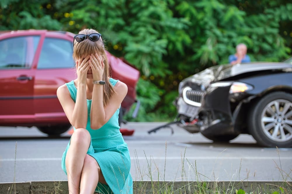 Distressed female driver sits on the roadside, visibly shocked, following a car accident in Albany, New York.