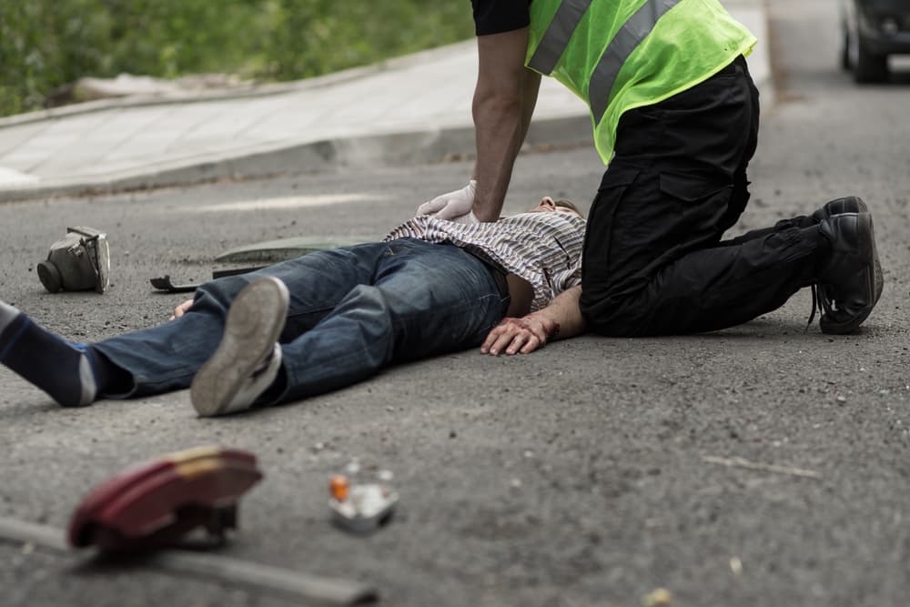 Image of a man performing CPR on a male victim of a car crash, administering life-saving measures at the scene.