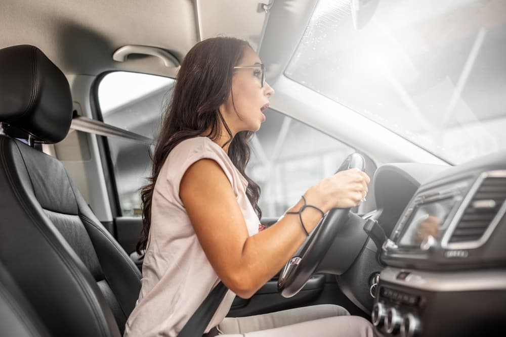 Inexperienced female driver sits close to the steering wheel, her mouth open in a frightened expression.