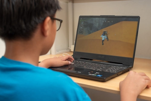 Boy playing Roblox on a laptop at a desk.