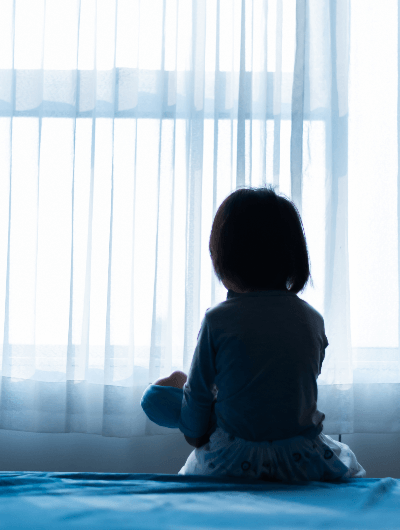 little girl on bed looking through curtains
