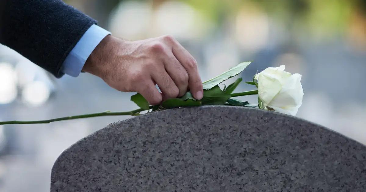 man's hand laying flower on tombstone