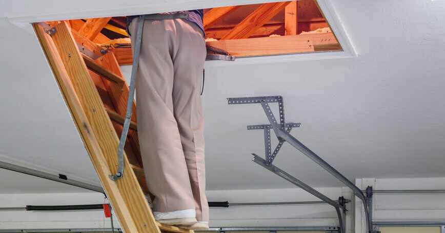 Person climbing a folding wooden attic ladder in a residential garage, illustrating the type of fall hazard involved in the Louisville Ladder recall.