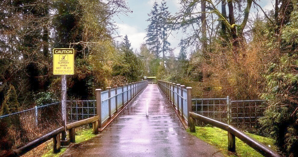 walking bridge in washington state with a yellow slippery when wet sign - Dolman Law Group