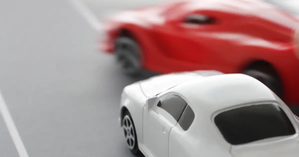 Improper lane change shown with a red toy car swerving near a white toy car.